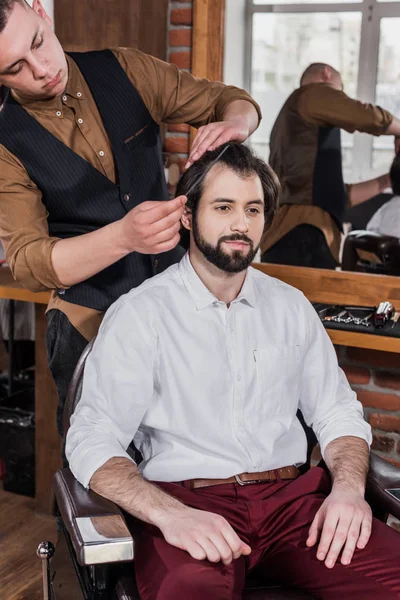 Giovane barbiere pettinando i capelli del cliente presso il barbiere — Foto stock