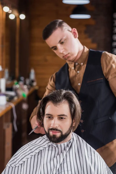 Barbudo joven conseguir corte de pelo de peluquero profesional en la barbería - foto de stock