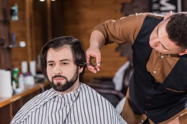 Joven guapo conseguir corte de pelo de peluquero profesional en la barbería - foto de stock