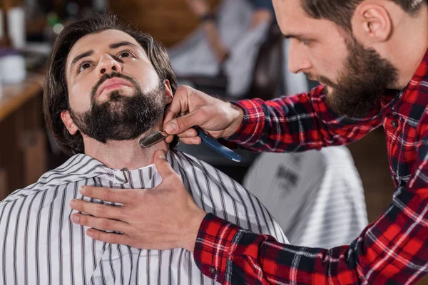 Close-up tiro de barbeiro jovem barbeando homem com máquina de corte de cabelo — Stock Photo