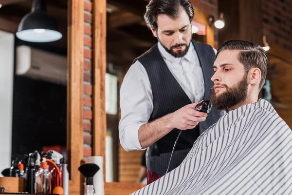 Bonito confiante barbeiro barbeando homem com máquina de corte de cabelo — Fotografia de Stock