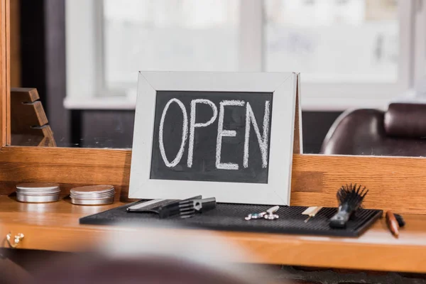 Tafel mit offenem Schild lehnt an Spiegel beim Friseur mit Werkzeug auf Gummimatte und Theke — Stockfoto
