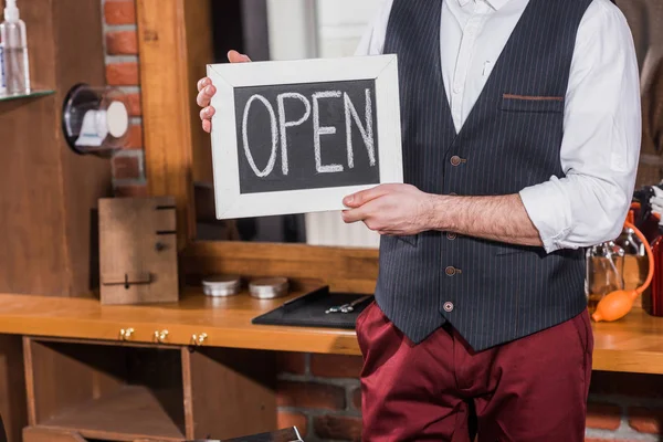 Cropped shot of barber holding open signboard in front of workplace — Stock Photo