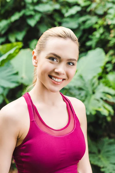 Nahaufnahme Porträt einer glücklichen jungen Frau in sportlichem Top, die im Park in die Kamera blickt — Stockfoto