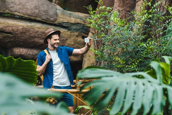 Joven guapo en ropa elegante tomar selfie en la selva tropical - foto de stock