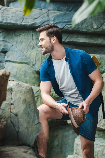Smiling young man in stylish clothes in front of rock in rainforest — Stock Photo