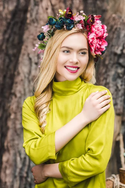 Feliz joven con corona floral con tronco de árbol borroso en el fondo - foto de stock