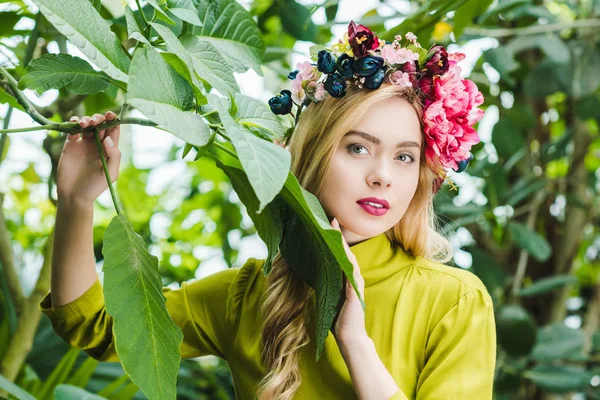 Hermosa mujer joven con corona floral mirando a la cámara en la selva tropical - foto de stock