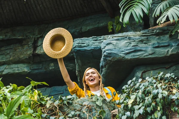 Bottom view of happy young woman waving with straw hat in jungle — Stock Photo