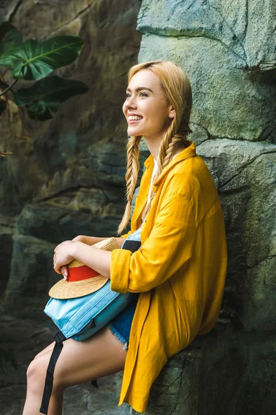 Smiling young woman in straw hat relaxing on rocks outdoors — Stock Photo