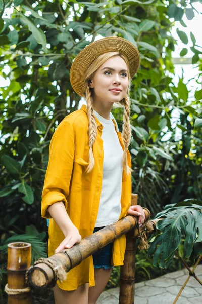 Atractiva mujer joven en sombrero de paja pasar tiempo en el jardín botánico - foto de stock