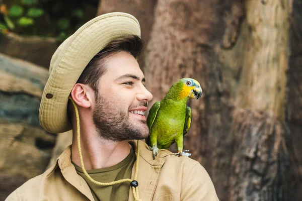 Schöner junger Mann mit Papagei auf der Schulter im Dschungel — Stockfoto