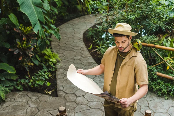 Beau jeune homme avec perroquet sur l'épaule et carte dans le parc jungle — Photo de stock