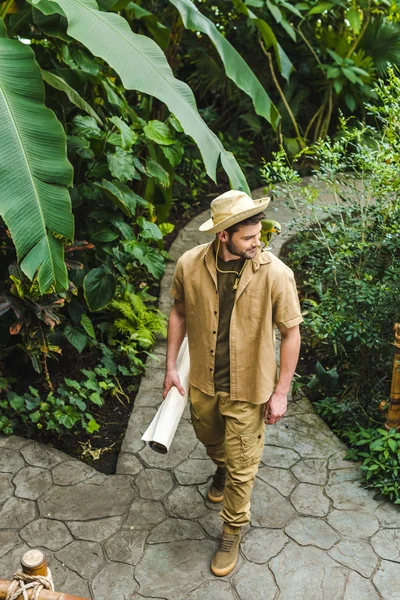 Joven guapo con loro en el hombro y mapa caminando por el parque de la selva - foto de stock