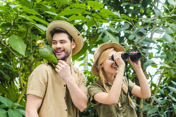 Feliz jovem casal com papagaio sentado no ombro do homem caminhadas juntos na selva — Fotografia de Stock