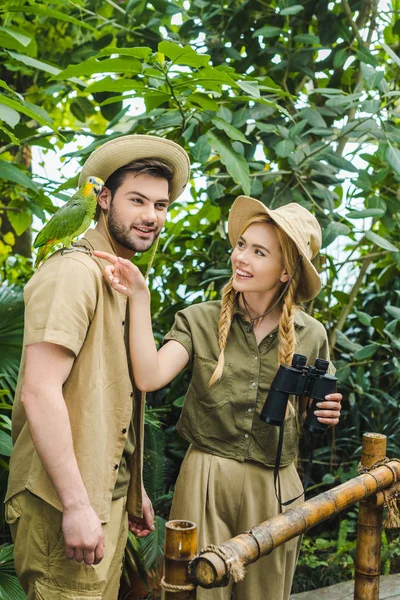 Atractiva pareja joven en trajes de safari con prismáticos caminando juntos en la selva tropical - foto de stock