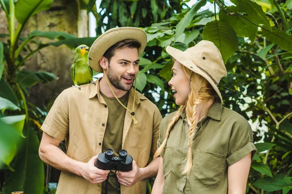 Beautiful young couple in safari suits with binoculars hiking together in rainforest — Stock Photo