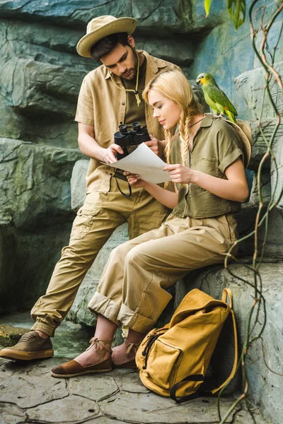Активная молодая пара в костюмах сафари с попугаем, путешествующим вместе — стоковое фото