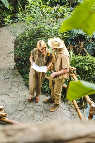 Vista de ángulo alto de la hermosa pareja joven en trajes de safari con mapa en la selva - foto de stock