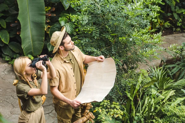 Schönes junges Paar in Safarianzügen mit Karte und Fernglas im Dschungel — Stockfoto