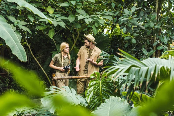 Привлекательная молодая пара в костюмах сафари, держащаяся за руки и путешествующая в джунглях — стоковое фото