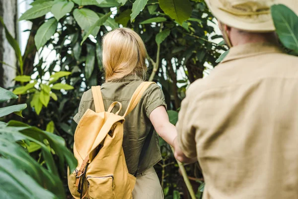 Rear view of young couple in safari suits holding hands and walking by in jungle — Stock Photo