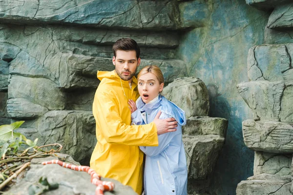 Jovem casal emocional em capas de chuva aterrorizado de cobra — Fotografia de Stock