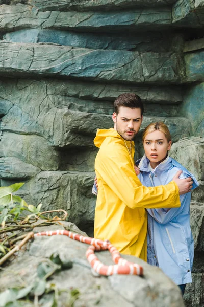 Frightened young couple in raincoats terrified of snake — Stock Photo