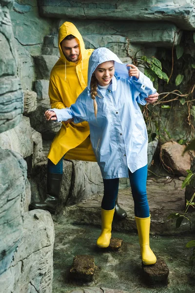 Happy young couple in raincoats walking by jungle — Stock Photo