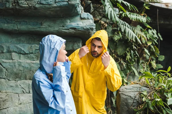 Atractiva pareja joven en impermeables en la selva - foto de stock