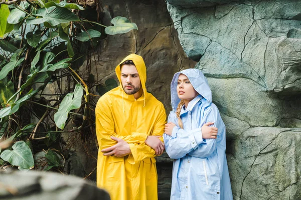 Congelado jovem casal em capas impermeáveis sob rochas na selva — Fotografia de Stock