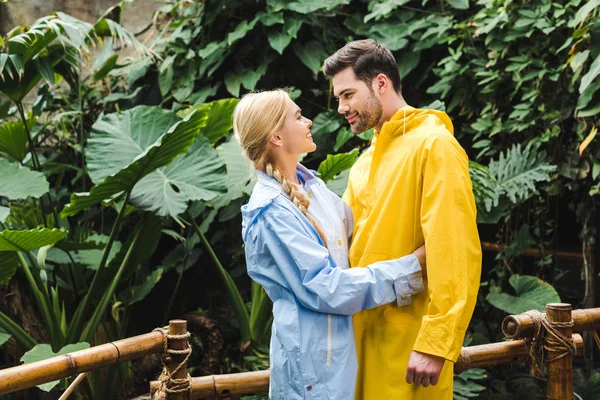 Beautiful young couple in raincoats embracing at rainforest — Stock Photo