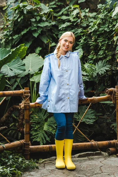 Bella giovane donna in impermeabile blu e stivali di gomma gialla nella foresta pluviale — Foto stock