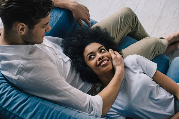 Man embracing African american girl while sitting on sofa — Stock Photo
