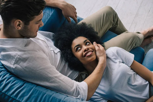 Mann umarmt afrikanisches amerikanisches Mädchen, während er auf dem Sofa sitzt — Stockfoto