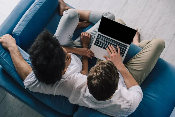 Casal multirracial sentado e no sofá e olhando para a tela do laptop — Fotografia de Stock