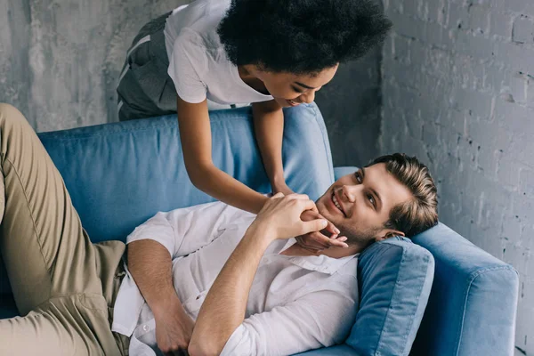 African american woman embracing man lying on sofa — Stock Photo