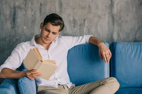 Hombre reflexivo leer libro mientras está sentado en el sofá - foto de stock