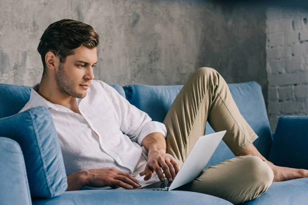 Man typing on laptop keyboard while lying on sofa — Stock Photo