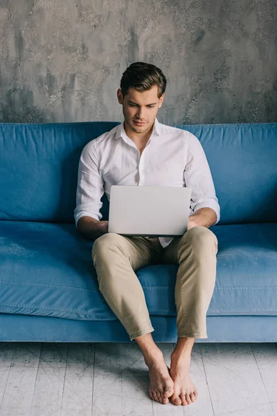 Young man working on laptop while sitting on sofa — Stock Photo