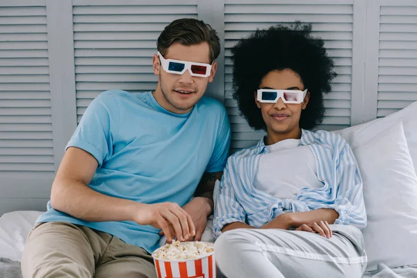 Мультирасовая пара в 3D очках смотрит кино дома с попкорном — стоковое фото