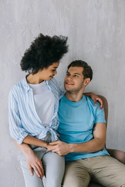 Jeune couple multiracial étreignant alors qu'il est assis sur une chaise — Photo de stock