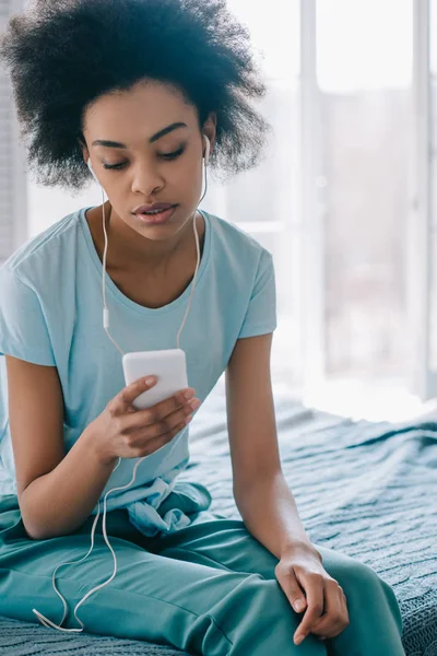 Молодая девушка сидит на кровати и слушает музыку по телефону — стоковое фото