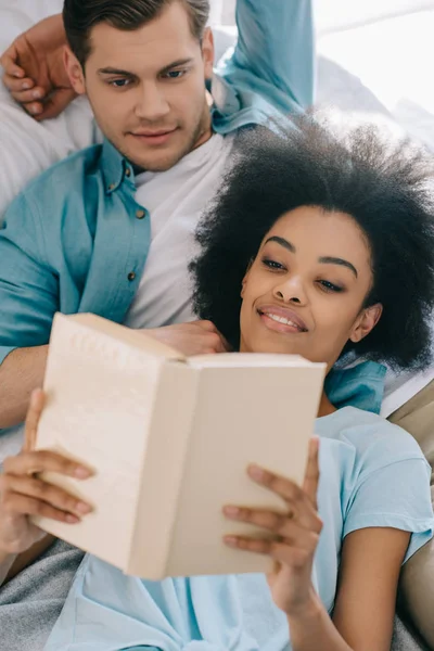 Relaxado casal leitura livro enquanto deitado na cama — Fotografia de Stock