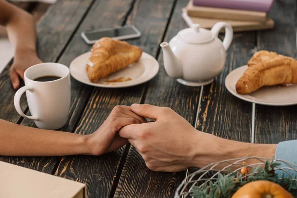 Vista close-up do casal de mãos dadas na mesa com café da manhã — Fotografia de Stock