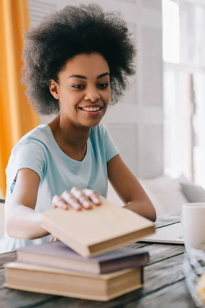 African american young woman choosing book from stack on table — Stock Photo