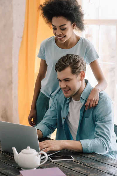 Multiracial boyfriend and girlfriend looking at laptop by the table — Stock Photo