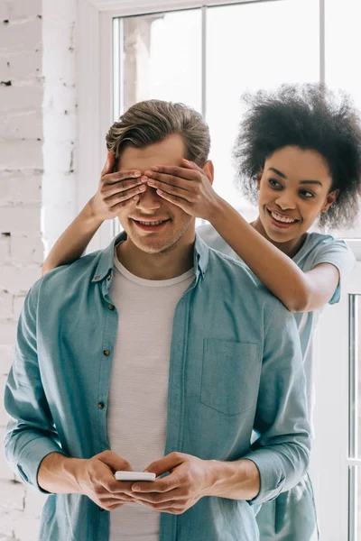 African american girl covering eyes of her boyfriend holding phone — Stock Photo