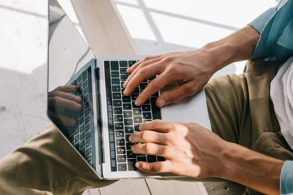 Vista de cerca del hombre escribiendo en el teclado del ordenador portátil en sus rodillas - foto de stock
