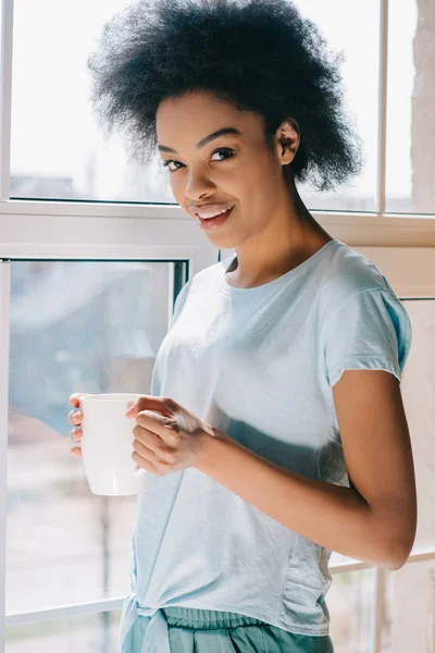 Sonriente chica afroamericana en el salón llevar taza de café - foto de stock